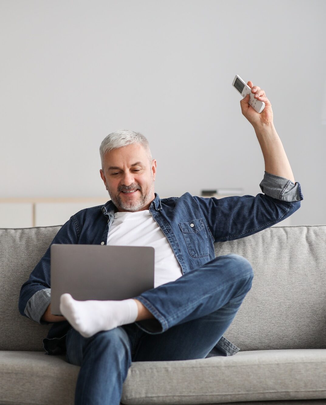 Relaxed man sitting on couch with laptop, turn on AC